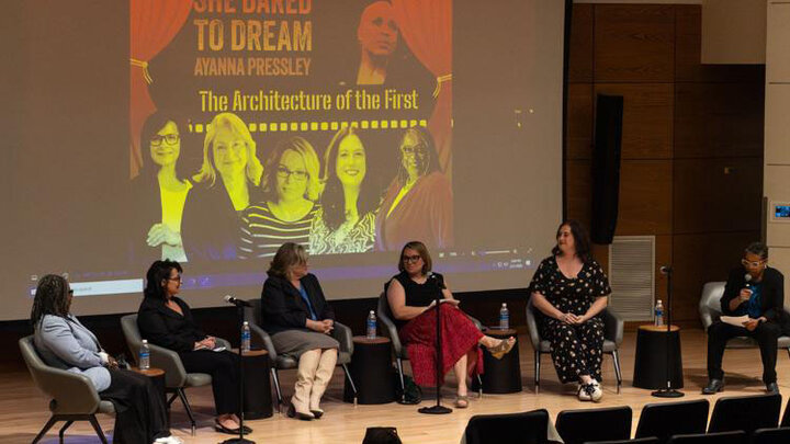 Panel discussion with six people seated on stage in front of a projected cover design.