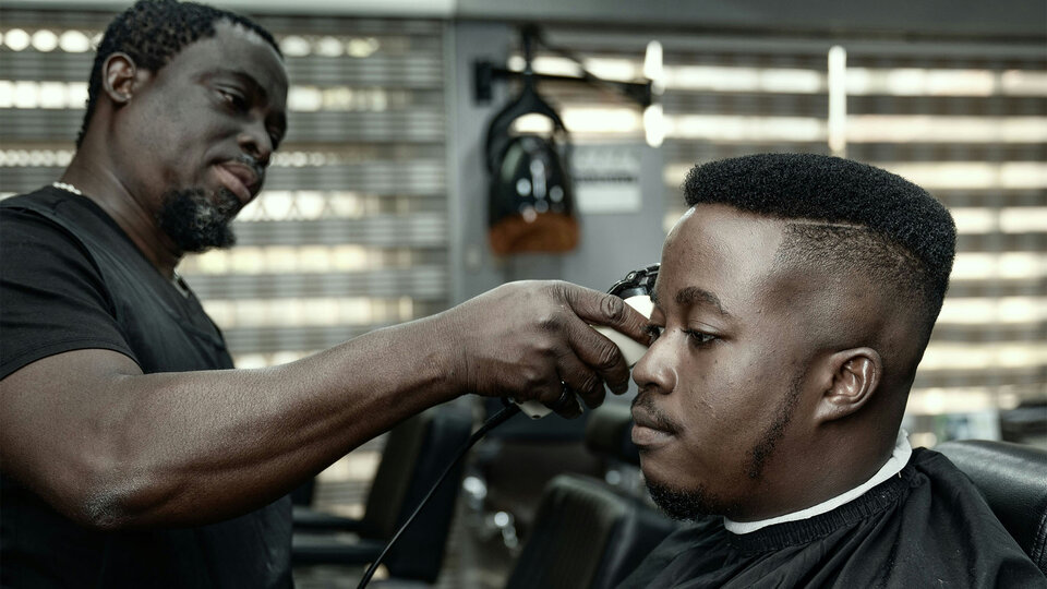 Barber trimming hair at a salon; modern hairstyle, well-lit interior with chairs and tools in the background.