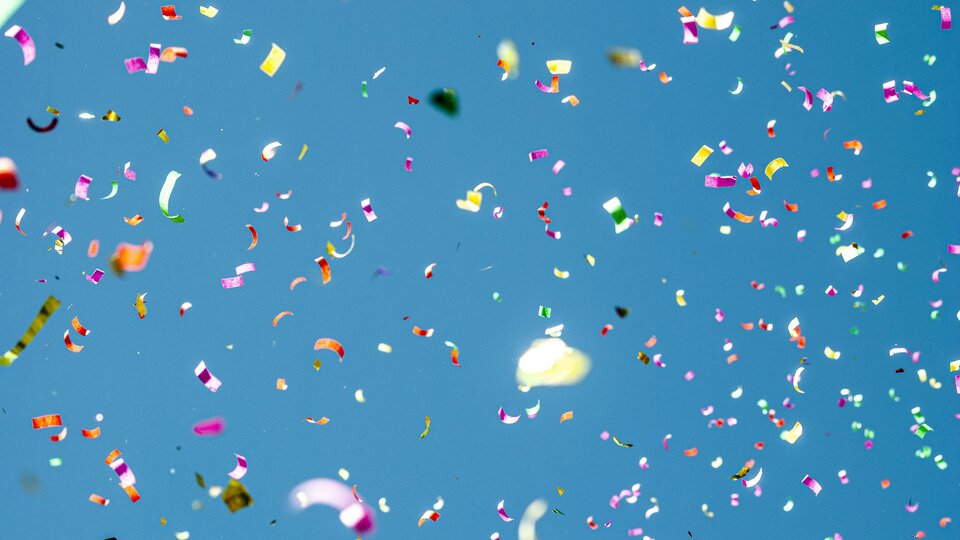Colorful confetti falling against a clear blue sky.